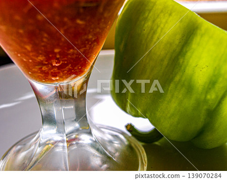 Extreme macro of tomato puree in a glass bowl with a green pepper slice. Detailed texture of thick sauce and emerald vegetable in a transparent creamer. High contrast food shot with reflections. Extreme macro of tomato puree in a glass bowl with a green pepper slice. Detailed texture of thick sauce and emerald vegetable in a transparent creamer. High contrast food shot with reflections. 139070284