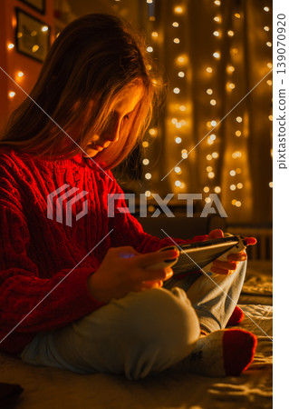 Vertical photo of a child focused on a video game with warm glowing garland lights in the background Vertical photo of a child focused on a video game with warm glowing garland lights in the background 139070920