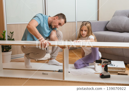 father and daughter carefully align furniture pieces together on the floor while surrounded by assembly tools and parts in a bright modern living room 139070922