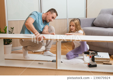 furniture assembly father and daughter together on the floor while surrounded by assembly tools and parts in a bright modern living room 139070924