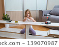 young girl sits among furniture parts on the floor, studying assembly instructions with tools and a screwdriver laid out before her in a bright living room 139070987