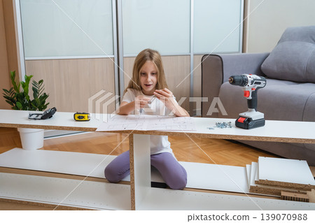 young girl sits among furniture parts on the floor, studying assembly instructions with tools and a screwdriver laid out before her in a bright living room young girl sits among furniture parts on the floor, studying assembly instructions with tools and a screwdriver laid out before her in a bright living room 139070988