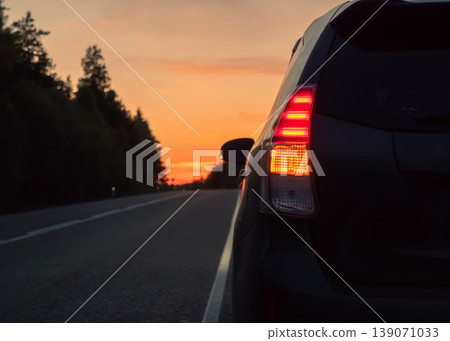 Rear view of dark vehicle with bright red taillights and amber turn signal on a road at sunset Rear view of dark vehicle with bright red taillights and amber turn signal on a road at sunset 139071033