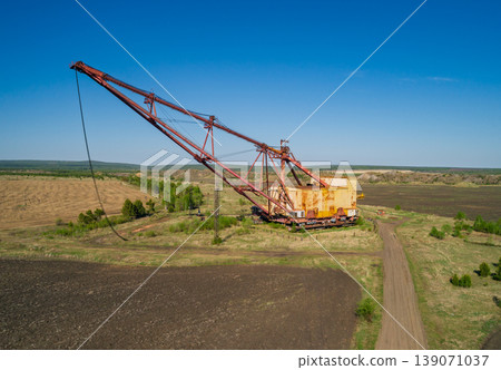 Massive industrial dragline excavator rests in an open field, surrounded by sparse vegetation and dirt roads Massive industrial dragline excavator rests in an open field, surrounded by sparse vegetation and dirt roads 139071037
