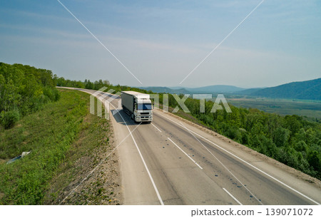Truck travels along a winding highway in a rural area with green hills under clear skies Truck travels along a winding highway in a rural area with green hills under clear skies 139071072