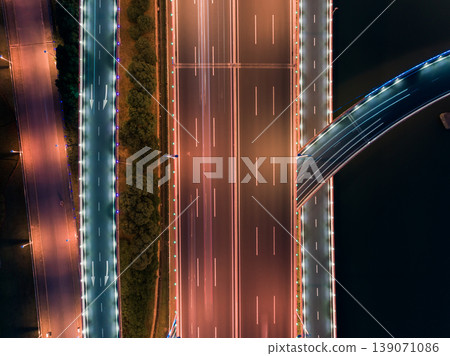 Illuminated modern highway and bridge infrastructure at night displaying light trails from urban traffic Illuminated modern highway and bridge infrastructure at night displaying light trails from urban traffic 139071086