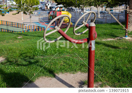 Outdoor fitness equipment with rotating handles situated in a grassy park area, playground structures visible in the background 139071915