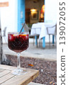 Refreshing cocktail in a crystal glass with fruit garnishes placed on a wooden table outside a restaurant with blue door in the background 139072055
