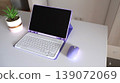 Purple laptop with keyboard and matching mouse on a white desk, accompanied by a small potted plant in a modern workspace setting 139072069