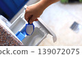 Hand holding a blue measuring scoop filled with detergent above a washing machine compartment in a bright laundry room setting 139072075