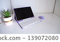 Modern purple laptop with white keyboard and matching mouse on a clean desk beside a small potted plant in a stylish container 139072080