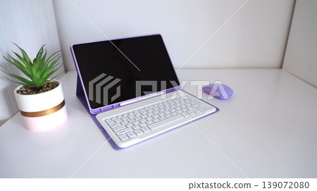Modern purple laptop with white keyboard and matching mouse on a clean desk beside a small potted plant in a stylish container Modern purple laptop with white keyboard and matching mouse on a clean desk beside a small potted plant in a stylish container 139072080
