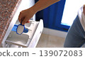 Person adding detergent to washing machine drawer in a bright laundry room with blue window and granite countertop 139072083