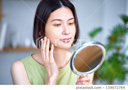 一位亞洲女性正在鏡子前檢查自己的皮膚狀況。 139072764