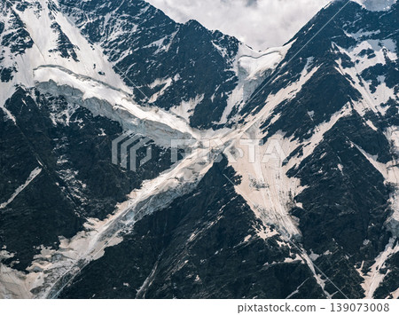 High altitude mountain range featuring steep, dark rock faces covered with extensive snow and ice. 139073008