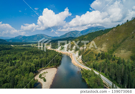 Mountain river meanders through a dense forest valley next to a winding road on a clear summer day Mountain river meanders through a dense forest valley next to a winding road on a clear summer day 139073068
