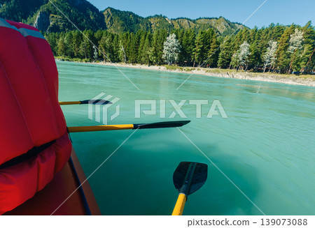 Paddling a raft on a vibrant turquoise river surrounded by dense green forests and majestic mountains under a clear sky Paddling a raft on a vibrant turquoise river surrounded by dense green forests and majestic mountains under a clear sky 139073088