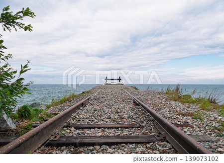 Old train tracks stretching to an endpoint barrier overlooking the calm sea on a cloudy afternoon 139073102