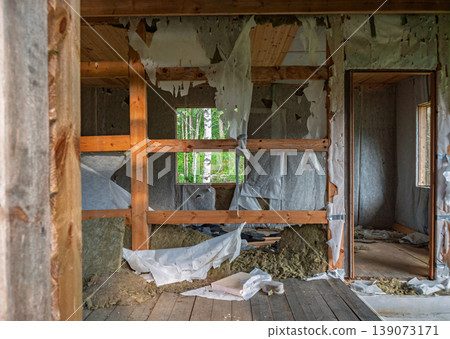 Interior view of an abandoned house with exposed wooden structural beams and torn wall insulation materials during daytime Interior view of an abandoned house with exposed wooden structural beams and torn wall insulation materials during daytime 139073171