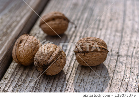 Closeup of four whole walnuts on aged wooden surface with natural textures and warm tones. Organic food, natural patterns, textures, and healthy nutrition. Copy space. Selective focus 139073379