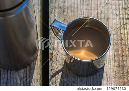Stainless steel camping thermos, metal cup, and group of walnuts on aged wooden surface. outdoor adventure, simplicity, minimalism, sustainability, and healthy snacking. Top view. Copy space 139073380
