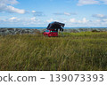 Red car with a rooftop tent parked near the sea, perfect for camping, adventure, and road trip lifestyle in nature. Outdoor exploration, freedom concept. Blue cloudy sky on background. Copy space 139073393