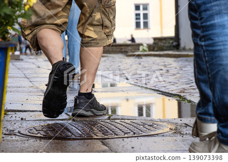 Closeup of men legs walking on a wet cobblestone street after rain, reflecting city architecture and urban lifestyle in Tallinn, Estonia, old town. Movement, footwear, rainy weather concept Closeup of men legs walking on a wet cobblestone street after rain, reflecting city architecture and urban lifestyle in Tallinn, Estonia, old town. Movement, footwear, rainy weather concept 139073398