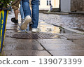 People walking on a wet cobblestone street after rain in an old town, Tallinn, Estonia. Pedestrians strolling on a historic city street with puddles reflecting movement and weather conditions 139073399