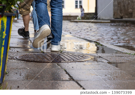 People walking on a wet cobblestone street after rain in an old town, Tallinn, Estonia. Pedestrians strolling on a historic city street with puddles reflecting movement and weather conditions 139073399