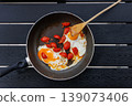 Overhead view of fried eggs cooked with cherry tomatoes in a frying pan on a black table with a wooden spatula. Simple home cooking and breakfast concept with copy space 139073406