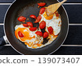 Overhead view of fried eggs cooked with cherry tomatoes in a frying pan on a black table with a wooden spatula. Simple home cooking and breakfast concept with copy space 139073407