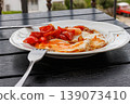 Side view close up of a fried egg served with cherry tomato on a white plate on a dark balcony table, with a fork in the foreground. Selective focus 139073410