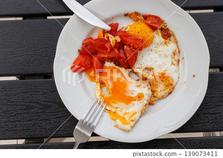 Fried eggs with cherry tomatoes served on white plate placed on a dark wooden table. Top view. Copy space Fried eggs with cherry tomatoes served on white plate placed on a dark wooden table. Top view. Copy space 139073411