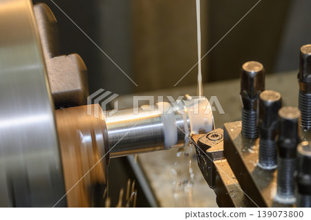 Heavy-duty lathe machine performing rough cutting on a metal shaft with high-pressure liquid coolant. 139073800