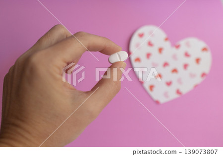 Hand holding a pill between his fingers. Background with blurred heart image. Hand holding a pill between his fingers. Background with blurred heart image. 139073807