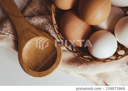 Farm fresh eggs in a rustic woven basket with a natural wooden spoon on a beige textile.Healthy nutrition and baking ingredients 139073968