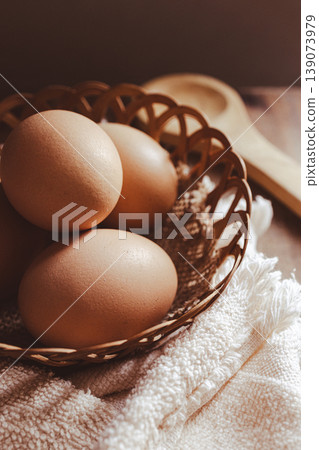 Farm fresh, brown organic eggs resting in a rustic woven basket on a white textured towel Farm fresh, brown organic eggs resting in a rustic woven basket on a white textured towel 139073979