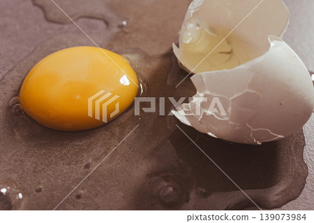 Cracked egg releasing its vibrant yolk and clear albumen onto a textured surface symbolizing fresh nutrition and healthy diet Cracked egg releasing its vibrant yolk and clear albumen onto a textured surface symbolizing fresh nutrition and healthy diet 139073984