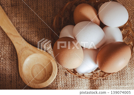Fresh whole eggs in a woven basket next to a wooden spoon , all placed on a burlap background. Rustic still life set Fresh whole eggs in a woven basket next to a wooden spoon , all placed on a burlap background. Rustic still life set 139074005