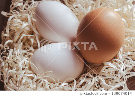 Three fresh chicken eggs laying in a nest of wood shavings, including two white eggs and one brown egg Three fresh chicken eggs laying in a nest of wood shavings, including two white eggs and one brown egg 139074014