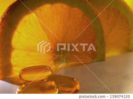 Vitamin C softgels in foreground.Oranges in background Vitamin C softgels in foreground.Oranges in background 139074120