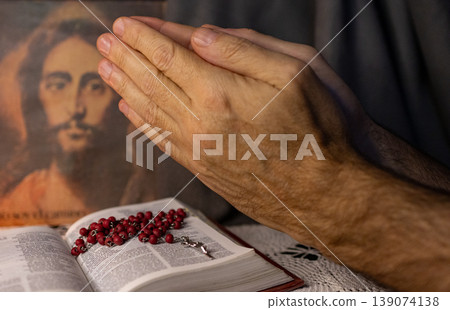 A man praying to the image of Christ. Bible and Rosary on his table 139074138