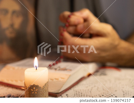 Lighted candle in front. Hands of a young man praying the rosary Lighted candle in front. Hands of a young man praying the rosary 139074157