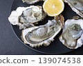 Khasan oysters, live, fresh, opened. Served with classic French Mignonette sauce and half a lemon. Blue plate, black background. Selective focus, close-up. 139074538