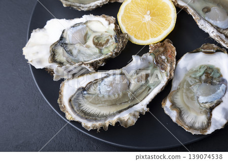 Khasan oysters, live, fresh, opened. Served with classic French Mignonette sauce and half a lemon. Blue plate, black background. Selective focus, close-up. Khasan oysters, live, fresh, opened. Served with classic French Mignonette sauce and half a lemon. Blue plate, black background. Selective focus, close-up. 139074538