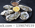 Khasan oysters, live, fresh, opened. Served with classic French Mignonette sauce and half a lemon. Blue plate, black background. Selective focus, close-up. 139074539