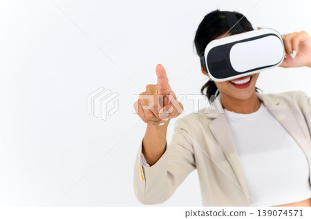 business woman in informal suit wearing VR goggles pointing in the air while standing isolated on white background. concept of Metaverse, virtual reality, future, technology, and internet of things. business woman in informal suit wearing VR goggles pointing in the air while standing isolated on white background. concept of Metaverse, virtual reality, future, technology, and internet of things. 139074571