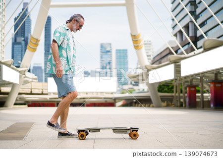 Happy senior Caucasian man with white beard and sunglasses walking on city skywalk while carrying electric skateboard. Concept of joyful aging, travel adventure, and the use of modern personal mobilit 139074673