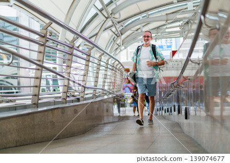 Happy senior Caucasian man with white beard and sunglasses walking on city skywalk while carrying electric skateboard. Concept of joyful aging, travel adventure, and the use of modern personal mobilit 139074677