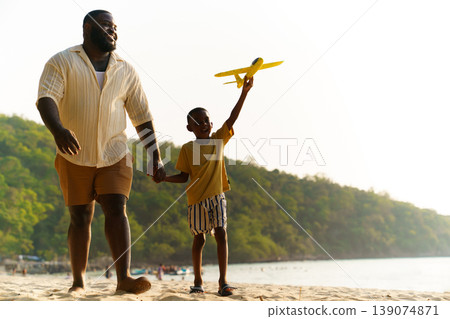 Joyful dad holding hands with kid playing toy airplane on sandy beach 139074871